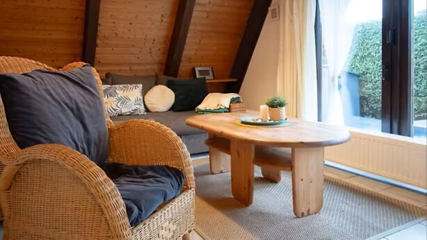 A cozy room with a wooden ceiling, a wicker sofa, a small table, and a window with curtains. - Family-friendly vacation home in Burhave - 500 m to the beach, WLAN, garden (Burhave)