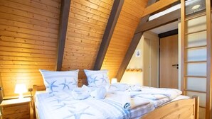 A bedroom with a wooden ceiling, a bed with white bedding, and a nightstand. - Family-friendly vacation home in Burhave - 500 m to the beach, WLAN, garden (Burhave)