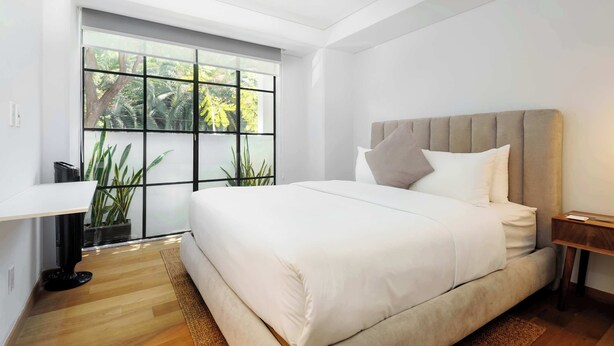 Une chambre moderne avec un grand lit, un bureau et une fenêtre donnant sur la verdure.