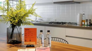 A kitchen with a wooden table, a vase with green plants, two water bottles, and a welcome card. - w* | Enchanting 2BR in the Heart of Roma Norte (Ciudad de México)