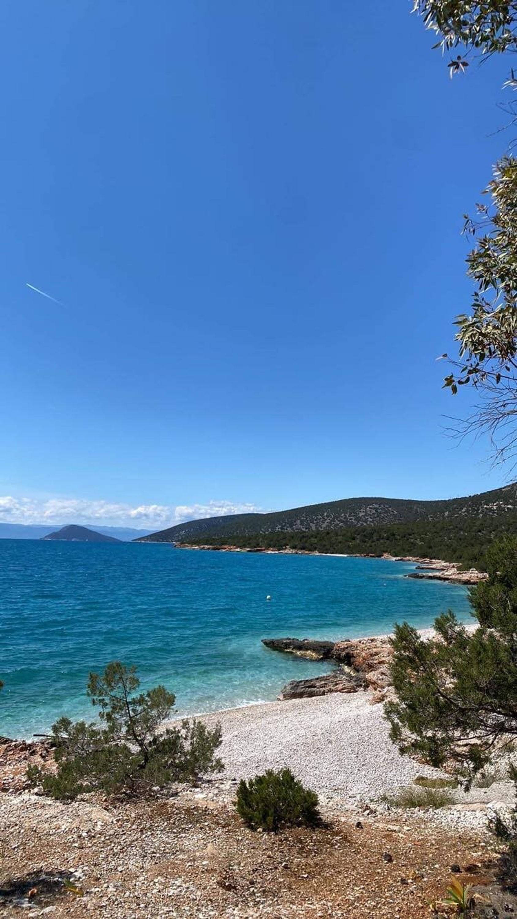 Eine Küstenlandschaft mit klarem, blauem Meer, felsigem Ufer und spärlicher Vegetation.