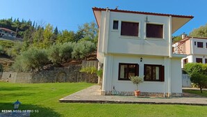 Ein zweistöckiges Haus mit einem kleinen Garten und einer Steinmauer im Hintergrund.