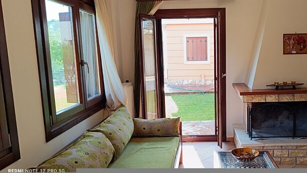 Ein Wohnzimmer mit einer Couch, einem Kamin und Blick auf einen Garten durch eine geöffnete Tür.