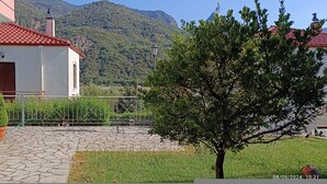 Ein Haus mit einer Steinterrasse, einem kleinen Garten und Bergblick.