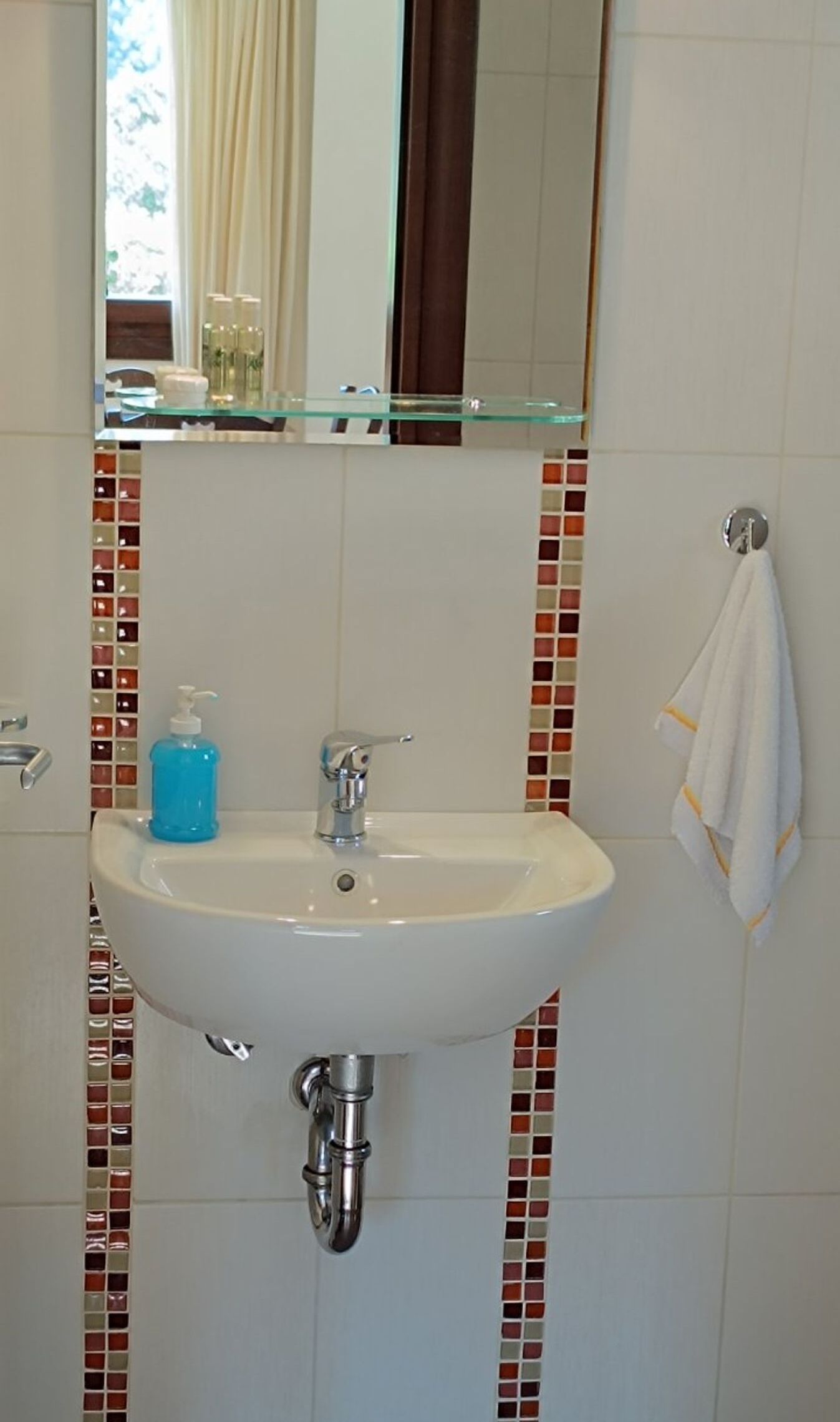 A bathroom with a white sink, chrome faucet, and a glass shelf above it.