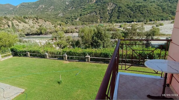 Uma varanda com vista para um jardim gramado, uma antena parabólica e montanhas ao fundo.