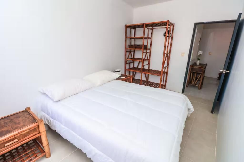 A bedroom with a bed, a wooden shelf unit, a small wooden table, and a door leading to another room.