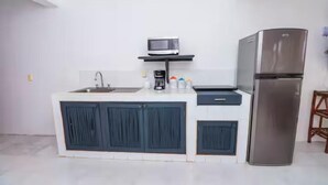 A modern kitchen with a stainless steel refrigerator, a microwave on a shelf, a sink, and cabinets. - Beachfront Olas Bungalow @Aqua at La Madera Beach. (Zihuatanejo)