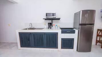 A modern kitchen with a stainless steel refrigerator, a microwave on a shelf, a sink, and cabinets.