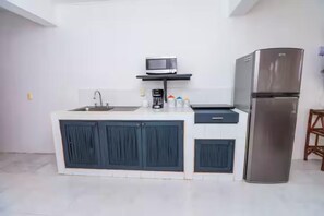 A modern kitchen with a stainless steel refrigerator, a microwave on a shelf, a sink, and cabinets.