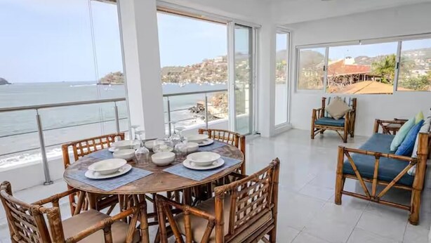 A dining area with a table set for six, overlooking a coastal view. - Beachfront Olas Bungalow @Aqua at La Madera Beach. (Zihuatanejo)