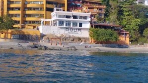 A coastal building with the sign "AQUA" on the side, adjacent to a rocky shoreline. - Beachfront Olas Bungalow @Aqua at La Madera Beach. (Zihuatanejo)