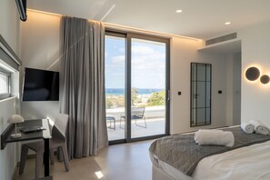 Ein modernes Hotelzimmer mit Bett, Schreibtisch, Sessel, Fernseher und einem Balkon mit Meerblick.