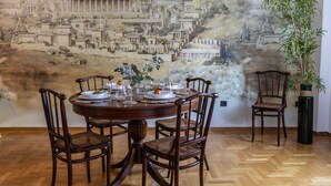 A dining area with a round table set for four, surrounded by wooden chairs, against a backdrop of a detailed mural depicting ancient architecture. - Acropolis Museum Retreat - 2 Bedroom Apartment (Athina)