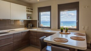A modern kitchen with a large island, dark wood cabinets, and a view of the sea. - Luxury  Villa  Kopsas (Kokkini Hani)