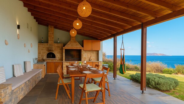An outdoor kitchen with a stone fireplace, wooden dining table, and chairs, overlooking a scenic ocean view. - Luxury  Villa  Kopsas (Kokkini Hani)