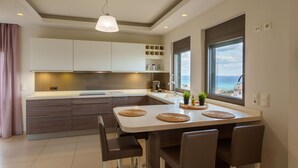 A modern kitchen with a central island, built-in cabinets, and a large window offering a view. - Luxury  Villa  Kopsas (Kokkini Hani)