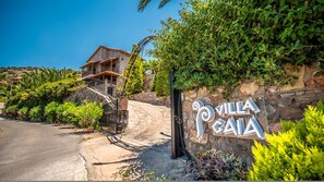Un mur de pierre sur lequel est inscrit le texte « Villa Gaia », et un escalier en pierre menant à une maison.