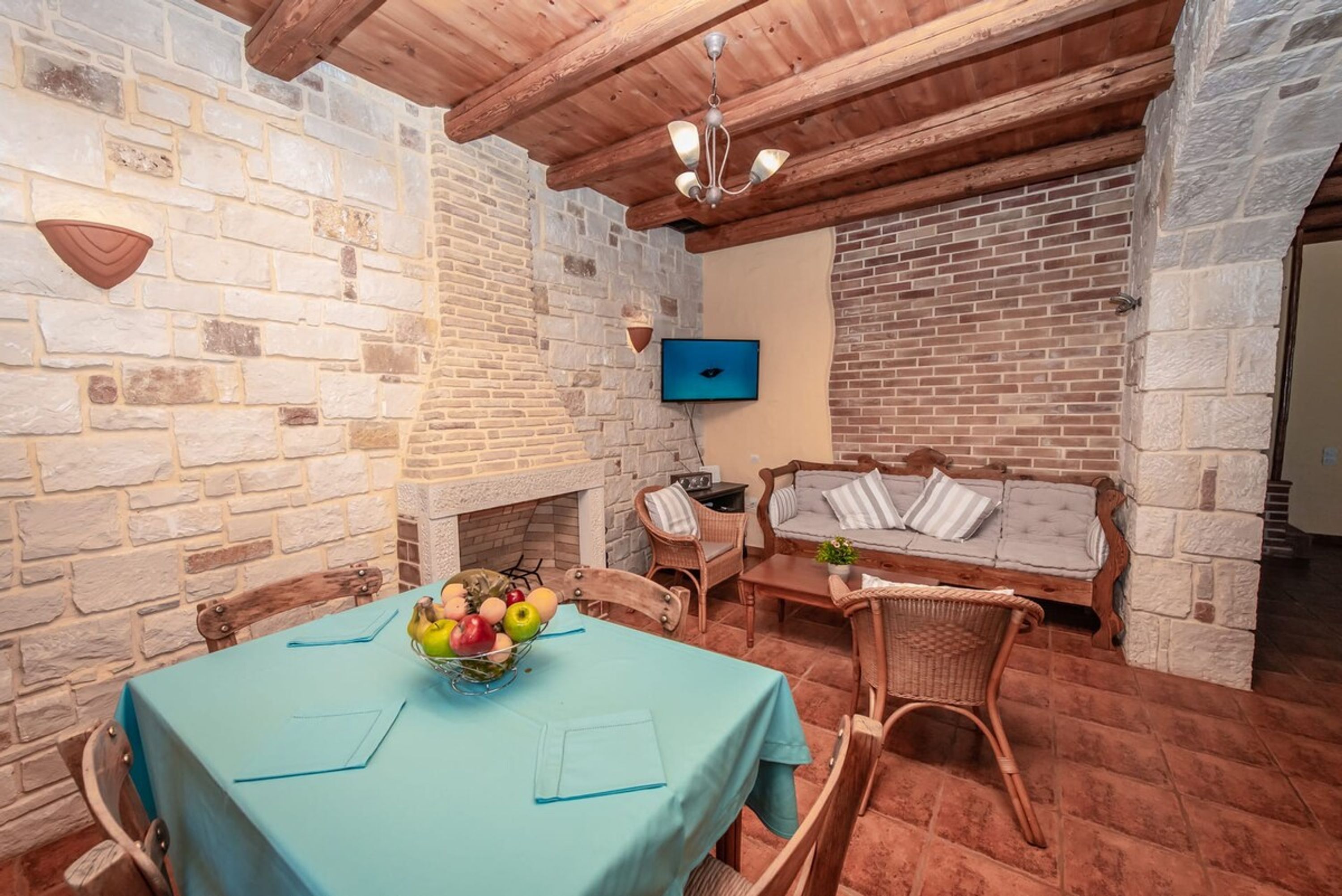 Un coin repas agrémenté d’un mur en pierre, d’un plafond en bois et d’une table sur laquelle est posé un panier de fruits.