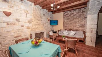 Un coin repas agrémenté d’un mur en pierre, d’un plafond en bois et d’une table sur laquelle est posé un panier de fruits.
