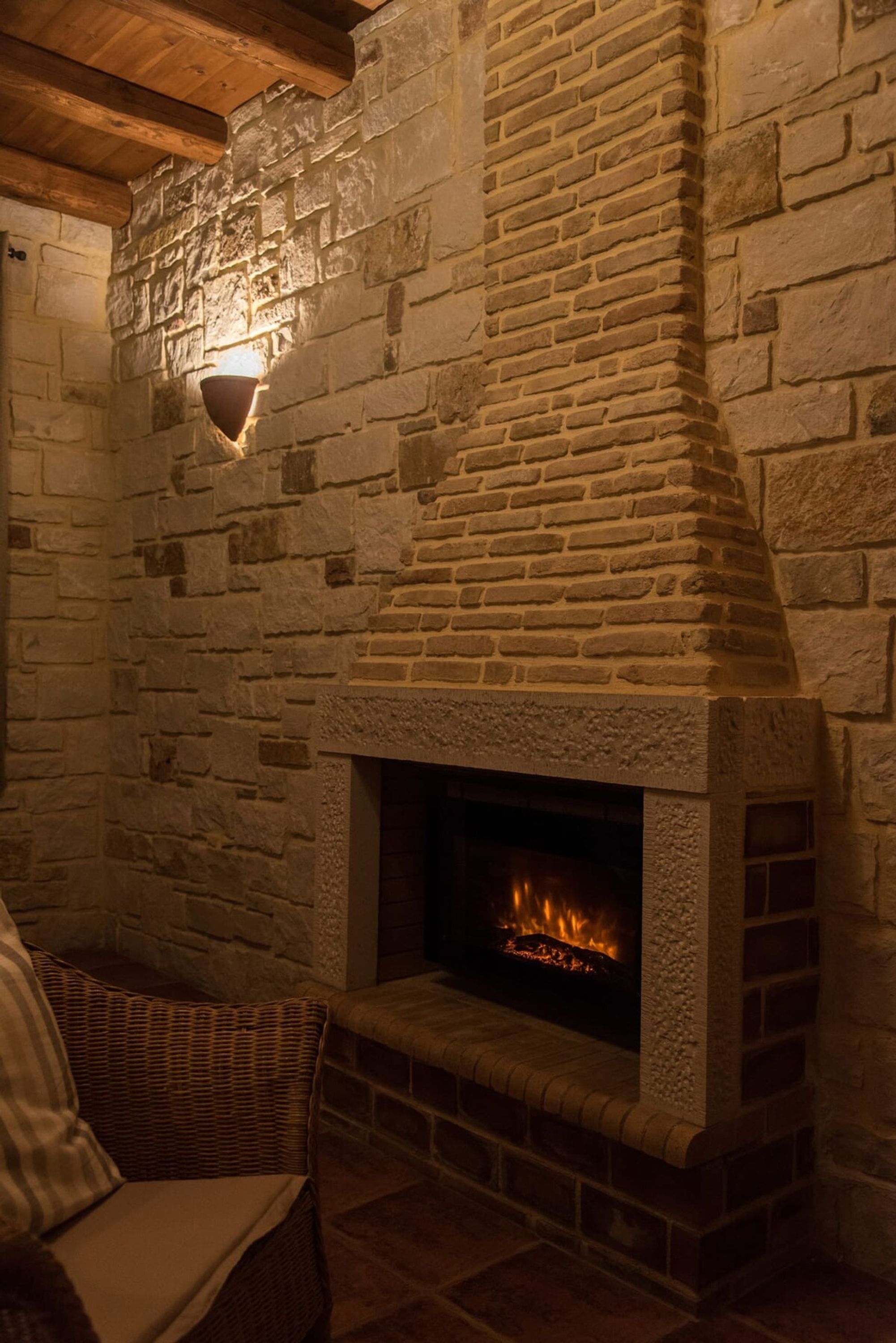 Une cheminée en pierre avec un feu de bois, un fauteuil en osier et un mur en pierre.