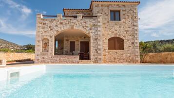 Une villa en pierre dotée d’une piscine, avec une entrée en arc de pierre et une terrasse.