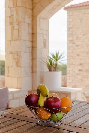 Un cuenco de frutas sobre una mesa de madera, con una pared de piedra y una planta en maceta al fondo.