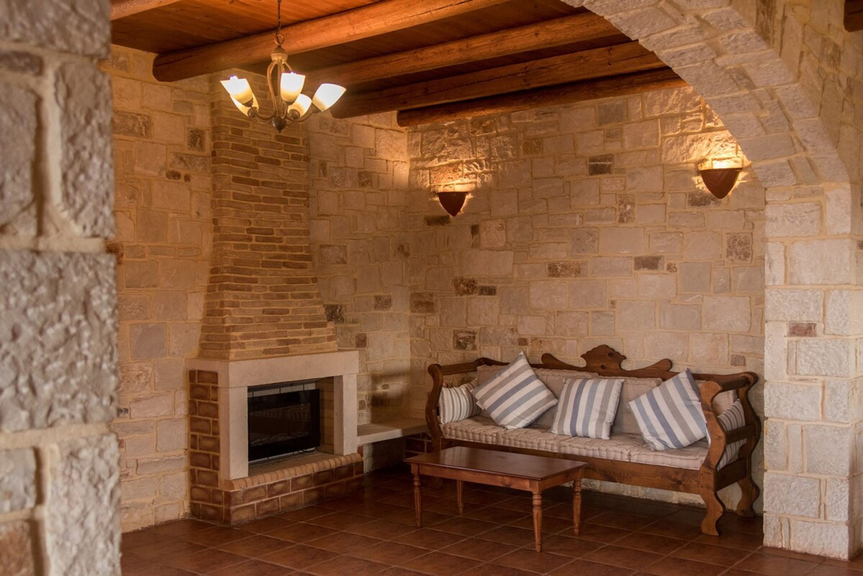 A stone-walled room with a fireplace, a wooden bench, and a cushioned sofa.
