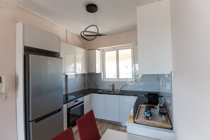 A modern kitchen with a stainless steel refrigerator, white cabinets, a black countertop, and a window providing natural light. - Athens Acropolis View Penthouse-Center of Athens (Athina)