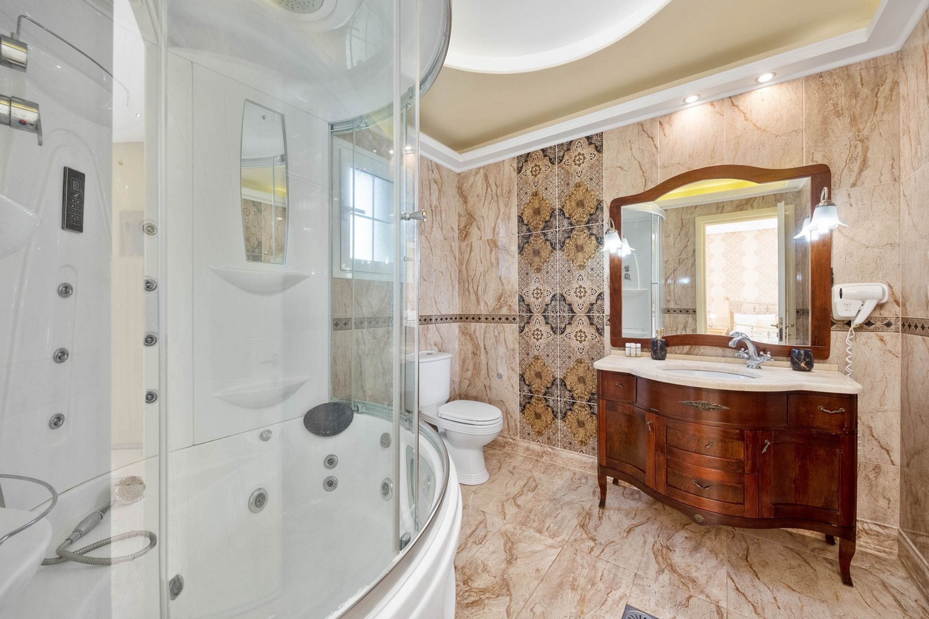 A bathroom with a glass-enclosed shower, a white toilet, a vanity with a mirror, and patterned tiles on the walls.
