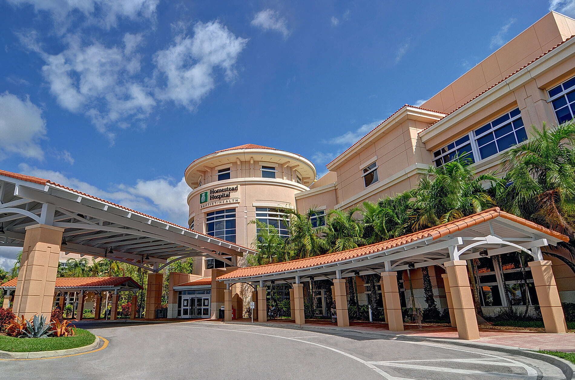 A hospital building with a circular central tower, covered walkways, and a landscaped entrance area.