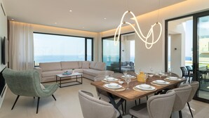 A modern living room with a dining area, large windows, and a view of the ocean. - Luxury  Villa  Verde (Agios Dimitrios Rodias)