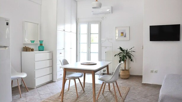 Een moderne, goed verlichte kamer met een eettafel, stoelen, een koelkast, een potplant en een flatscreen televisie.