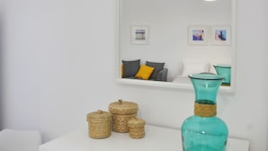 Een witte kamer met een grote spiegel, rieten manden en een tealvaas op een witte tafel.
