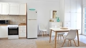Een moderne keuken met witte kastjes, een magnetron, een oven en een koelkast. Er staat een eettafel met stoelen en een vloerkleed.