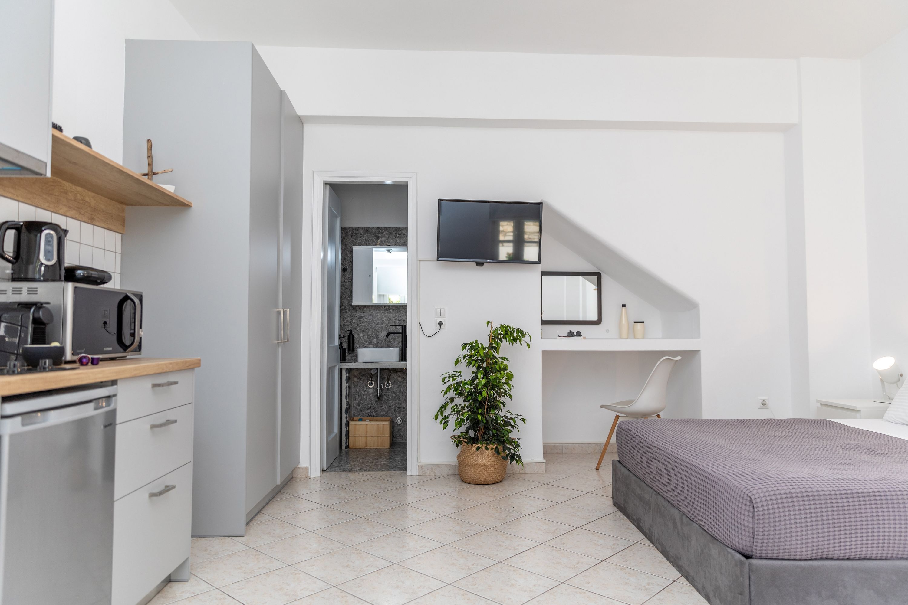A modern, compact room with a kitchenette, a bed, a desk, and a TV.