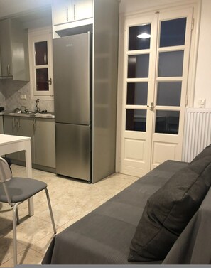 A compact kitchen with a refrigerator, a dining table with a chair, and a sofa in the living area. - One Bedroom Apartment (Naxos)