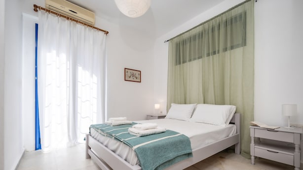Un dormitorio ordenado con cama, mesitas de noche y una ventana con cortinas.