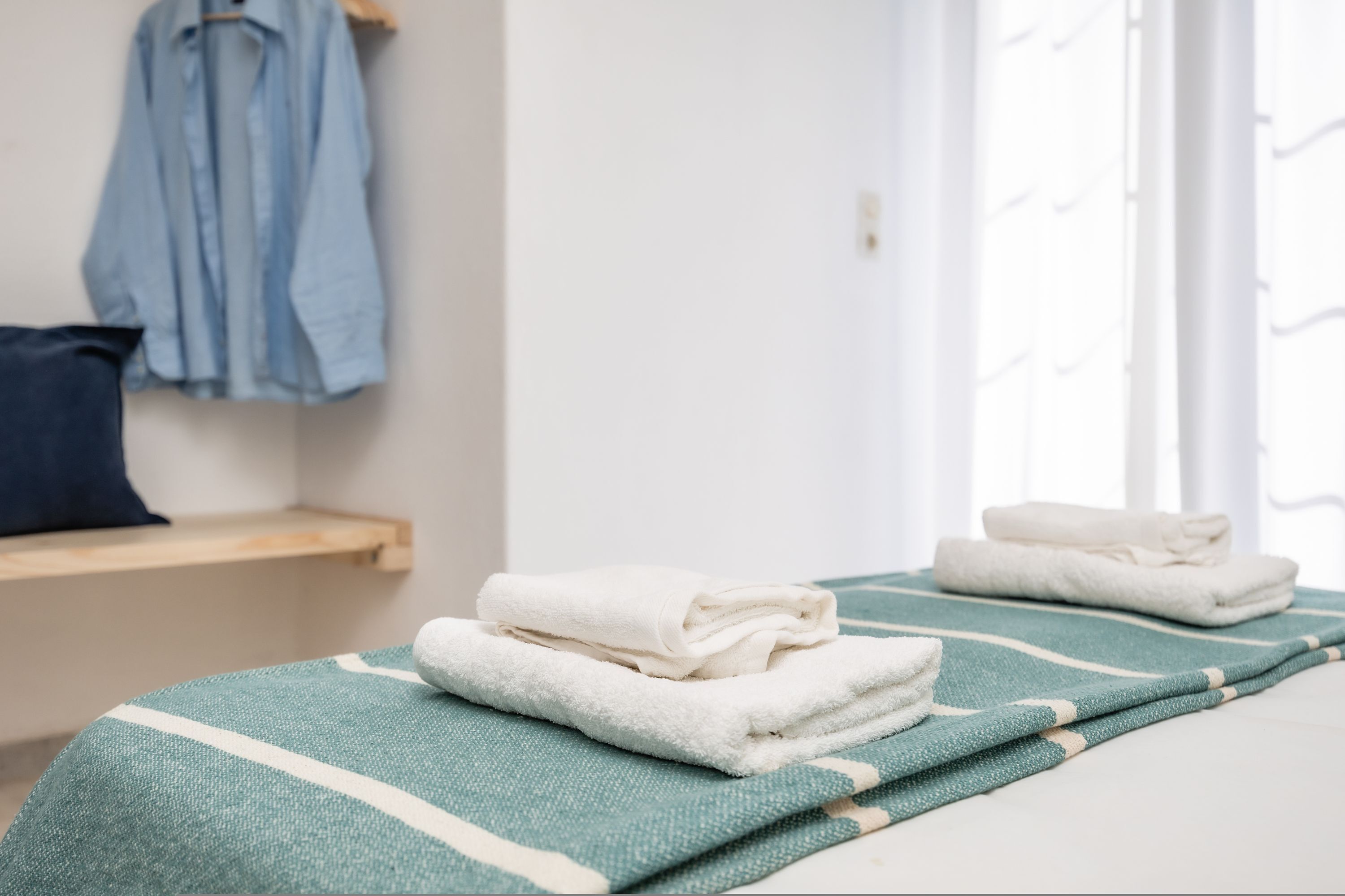 Een netjes opgemaakt bed met een groen-wit gestreept dekbed en gevouwen witte handdoeken.