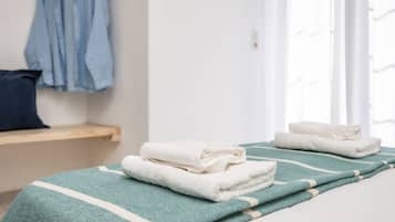 Een netjes opgemaakt bed met een groen-wit gestreept dekbed en gevouwen witte handdoeken.