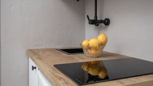 Una encimera de cocina con superficie de madera, un grifo negro, un bol de vidrio con limones y una tableta negra.