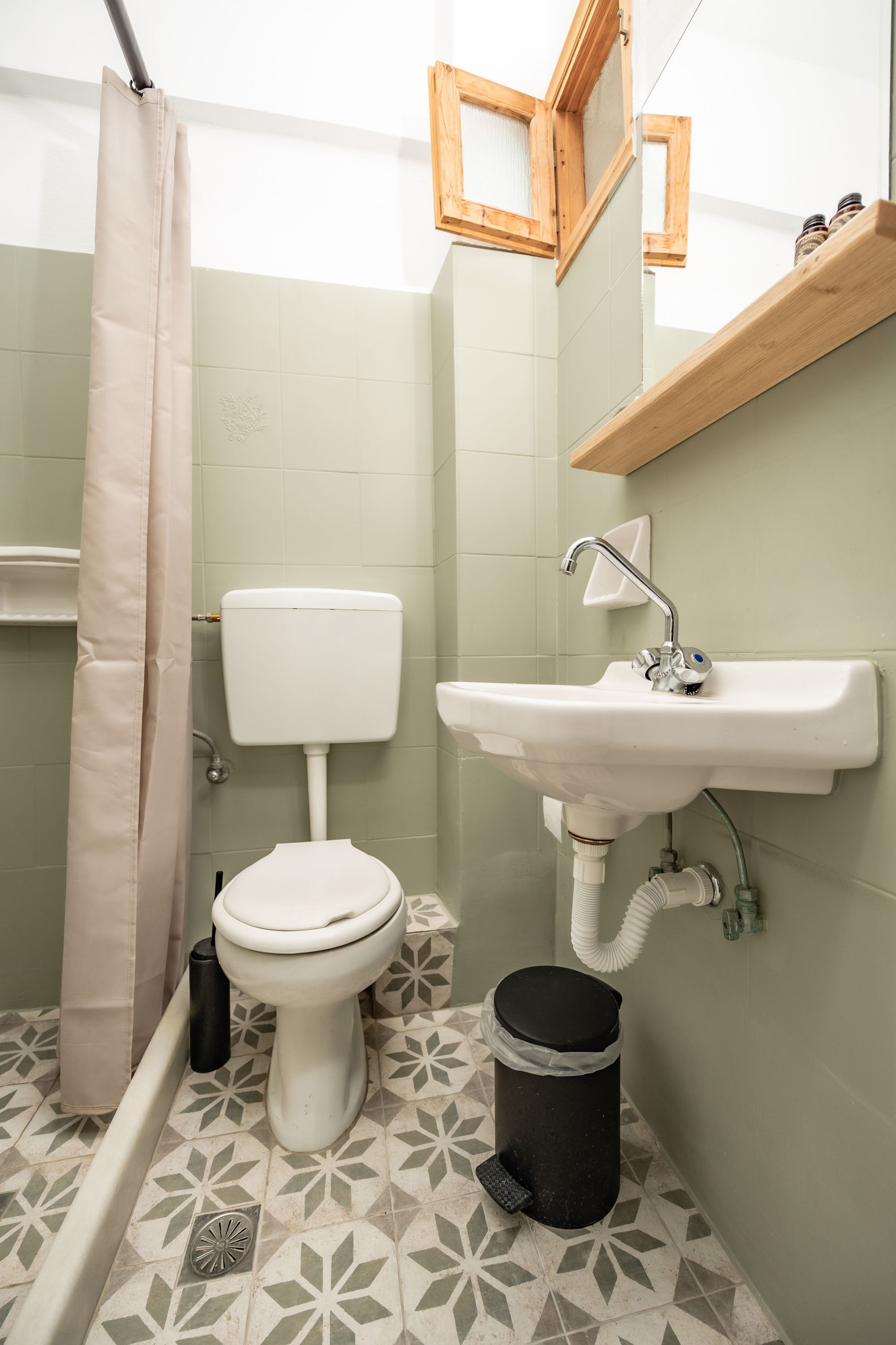 Een badkamer met toilet, wastafel, douchegordijn en een prullenbak.