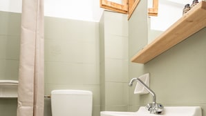 Un baño con inodoro, lavamanos, cortina de ducha y un cubo de basura.