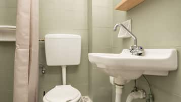 Een badkamer met toilet, wastafel, douchegordijn en een prullenbak.