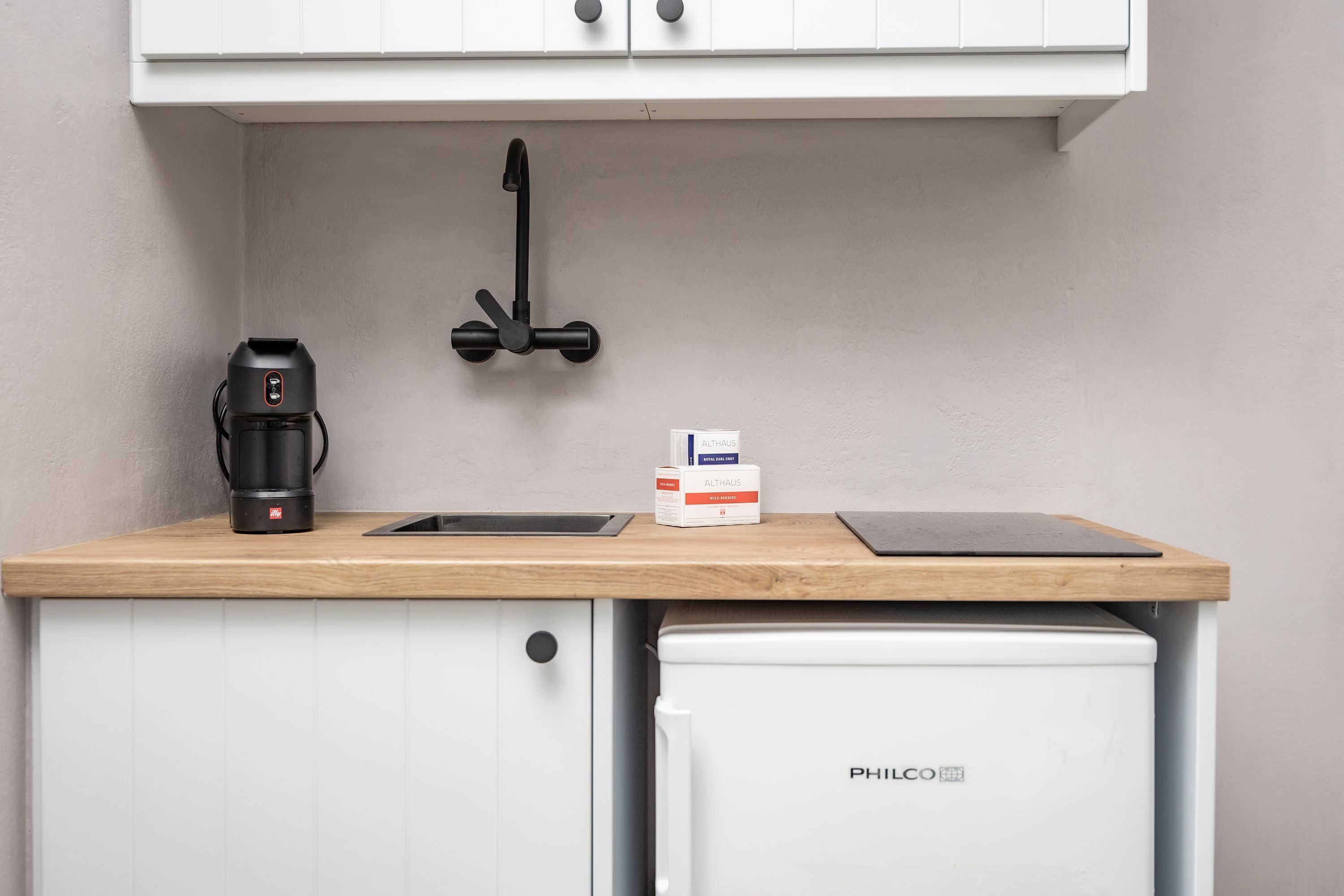 A compact kitchen with a coffee maker, a box of coffee pods, and a PHILCO refrigerator.
