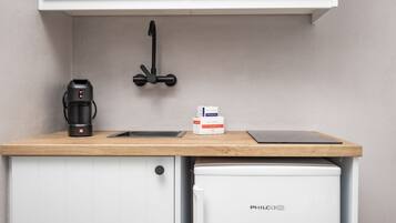 A compact kitchen with a coffee maker, a box of coffee pods, and a PHILCO refrigerator.