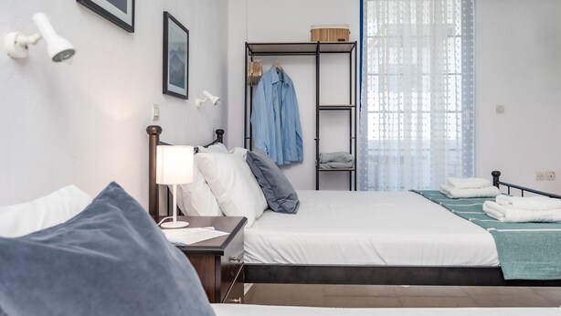 A modern hotel room with a large bed, a bedside table with a lamp, a wardrobe, and a view of the outdoors through sheer curtains. - Hippocampus - Standard Triple Studio (Moutsouna)