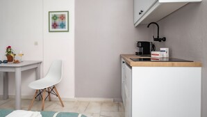 A small kitchenette with a white countertop, a coffee machine, and a sink. There is a white chair and a table with a potted plant and a glass of wine. - Hippocampus - Standard Triple Studio (Moutsouna)