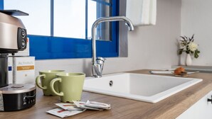 Una cuina moderna amb una màquina de cafè, dues tasses verdes i un rentaplat amb acabats blancs.