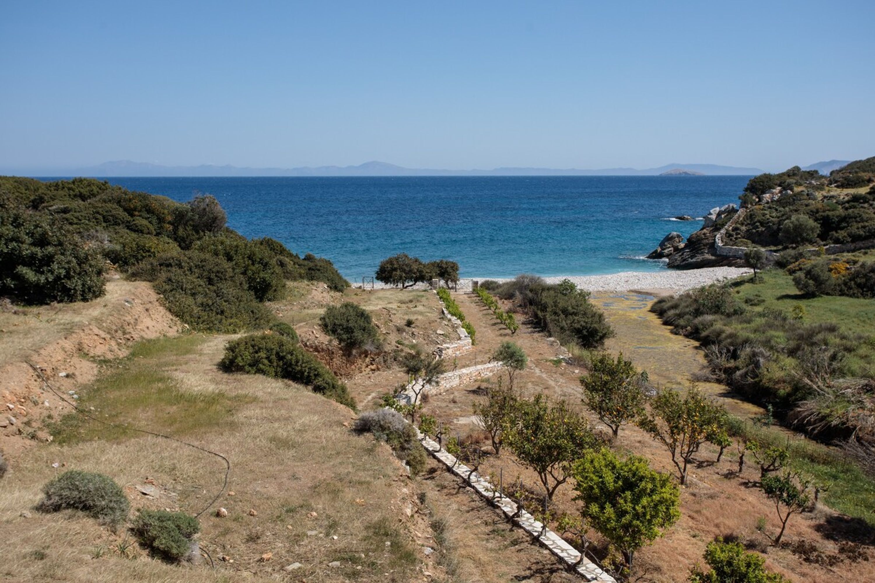 Un paisaje costero con vista despejada al mar, un sendero de tierra y vegetación escasa.